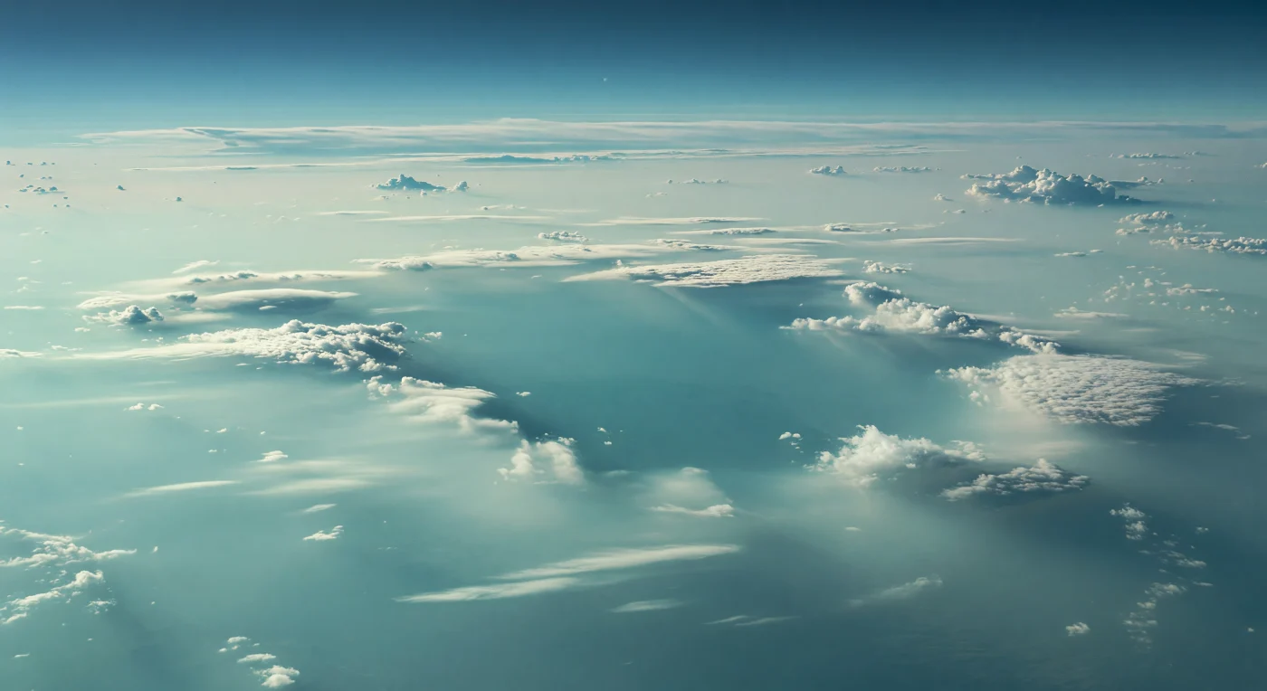 Une vaste déchirure s’ouvre dans les couches supérieures de nuages, comme une fenêtre continentale suspendue dans l’atmosphère, laissant voir bien plus bas une strate bleu sarcelle sombre qui absorbe la faible lumière et semble plonger dans un abîme sans fond. Tout autour, les bords de la faille nuageuse s’effilochent en bancs blanc pâle et cyan laiteux, probablement formés d’aérosols glacés de méthane et d’ammoniac, tandis que des nappes de brume stratifiée, des filaments de condensation et de subtils dômes convectifs donnent du relief à cet océan entièrement gazeux, sans sol ni horizon solide. La lumière, venue d’un Soleil réduit à un minuscule point diffus dans la brume bleu-vert, est froide, très dispersée et presque sans ombres, rehaussant à peine de reflets argentés les marges du gouffre tandis que les profondeurs se saturent de turquoise sombre et de bleu-vert assourdi sous l’effet de l’absorption du méthane. Face à ces terrasses de nuages qui s’étagent jusqu’à disparaître dans la brume, on ressent l’échelle immense et étrangère d’une atmosphère où la “surface” n’existe pas, seulement des couches qui s’enfoncent vers des fluides de plus en plus denses sous un ciel laiteux et silencieux.