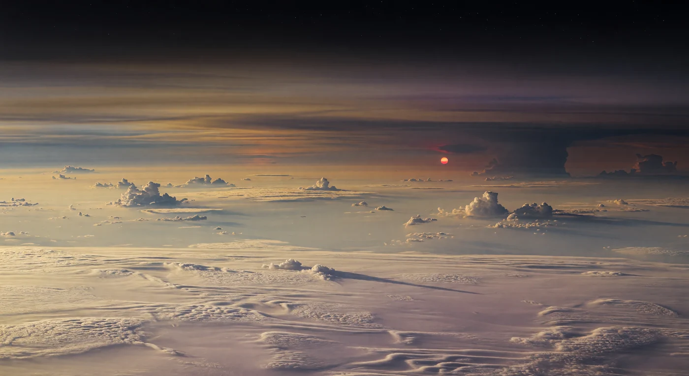 À la lisière du jour et de la nuit, on survole un océan de nuages crème et beige pâle dont les rides, sculptées par les vents, évoquent des dunes de vapeur s’étendant jusqu’à la courbure de l’horizon, tandis que d’immenses panaches convectifs jaillissent comme des chaînes de montagnes faites de brume. Ici, il n’y a aucun sol : seulement les hautes couches d’une géante gazeuse froide, dominée par l’hydrogène et l’hélium, où des nuages d’eau, d’ammoniac et d’hydrosulfure d’ammonium se superposent sous des voiles stratifiés bleu-gris, ambrés et mauves, faiblement éclairés par une petite étoile rouge orangée restée seule au ras de l’horizon après le coucher de sa compagne plus brillante. Cette lumière rubis, très faible et rasante, allonge d’un seul trait des ombres rougeâtres sur les ondulations lavande-taupe des sommets nuageux, tandis qu’un discret après-glow orangé persiste ailleurs au bord du ciel, trahissant la géométrie mouvante d’un système à deux soleils. Au-dessus, le ciel devient presque noir, à peine adouci par une brume de haute altitude et quelques étoiles timides, ce qui renforce l’impression saisissante de flotter dans une atmosphère profonde, glacée et immense, suspendu au-dessus d’un crépuscule que seule une planète sans terre ferme peut offrir.