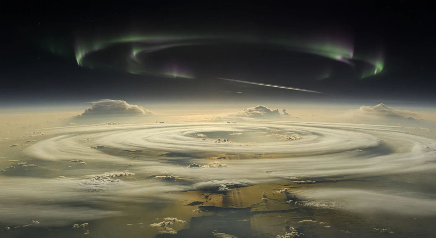 眼下に広がるのは地表ではなく、アンモニア氷の雲頂と薄い光化学ヘイズが幾重にも重なった、蒸気の海のような極域の雲景で、淡いクリーム色や鈍い金色の層の切れ目には、さらに深いアンモニウム水硫化物雲層の暗いオリーブ褐色の谷がのぞいています。黒に近い極夜の空の低い縁には、上層大気で散乱したバタースコッチ色のかすかな霞が帯のようにたなびき、その上を磁気圏に導かれた荷電粒子が生むオーロラが、柔らかな緑に紫やマゼンタの縁取りを伴う半透明の弧として極冠をなぞります。はるか遠くには、数百キロメートル規模の対流雲ドームがぼんやりと盛り上がり、強風に引き伸ばされた薄雲が巨大な惑星の曲率を際立たせ、ここが岩も海もないガス巨星の上層大気であることを実感させます。斜めに走る輪は、遠い太陽光をわずかに返す幽かな白灰色の細線にすぎず、気温およそ95ケルビンの凍てつく薄明の中で、静寂そのものが天文学的なスケールで頭上に広がっています。